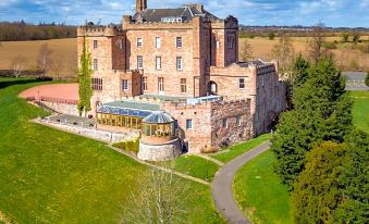 aerial view of a large brick castle surrounded by green fields and trees , with a swimming pool visible in the distance at Dalhousie Castle Hotel