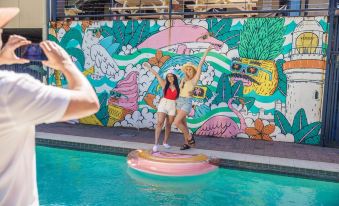 two young women posing for a photo in front of a colorful mural on the side of a swimming pool at YHA Byron Bay