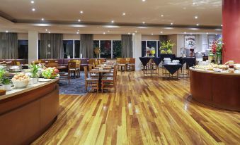 a large dining room with wooden tables and chairs , and a buffet table filled with various food items at Novotel Perth Langley