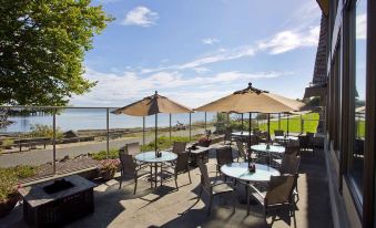 a patio area with tables , chairs , and umbrellas overlooking a body of water under a blue sky at Red Lion Hotel Port Angeles Harbor