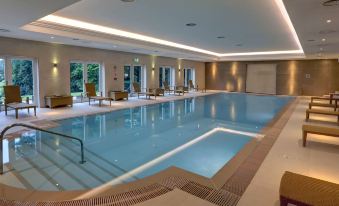 an indoor swimming pool surrounded by chairs and a lounge area , with people enjoying their time in the water at Best Western Lamphey Court Hotel