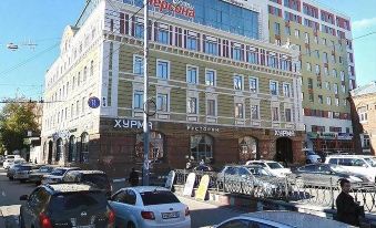 a city street with a tall building on the left side and several cars parked along the road at Diplomat Hotel