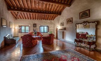 a spacious living room with wooden floors and high ceilings , featuring two red armchairs and a persian rug at Villa Campestri Olive Oil Resort