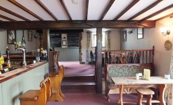 a cozy pub with wooden benches , tables , and chairs , as well as a bar area with stools and wine glasses at The Babbling Brook