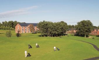 a group of people are playing golf on a grassy field near a building and trees at Macdonald Hill Valley Hotel, Golf and Spa