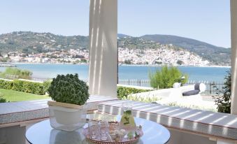 a table with a cake and a vase of flowers is set on a patio overlooking the ocean at Skopelos Village Hotel