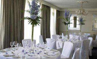 a well - decorated dining room with white tablecloths , chairs , and a centerpiece of tall blue flowers at Chilston Park Hotel
