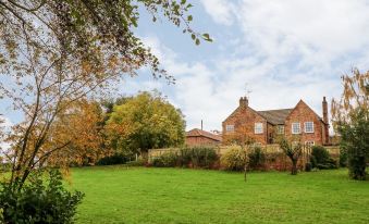 a brick house surrounded by a grassy field , with trees and bushes in the background at Travelodge Scotch Corner Skeeby