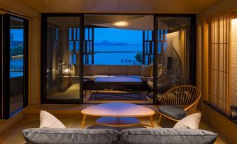 a living room with a couch , chairs , and a dining table in front of a large window overlooking the water at Biwako Ryokusuitei
