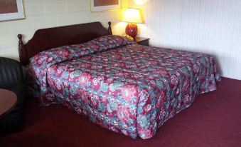 a bed with a floral comforter and pillows is shown in a room with red carpet at H&K Motel