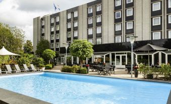 a hotel with a large outdoor pool surrounded by chairs and tables , as well as a tennis court nearby at Novotel Maastricht