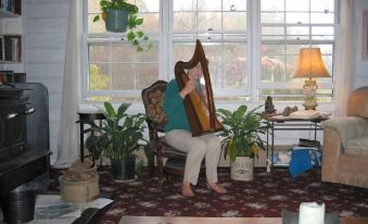 a woman is sitting on a couch playing a harp in a living room , surrounded by potted plants at Sylvan Falls Mill B&B