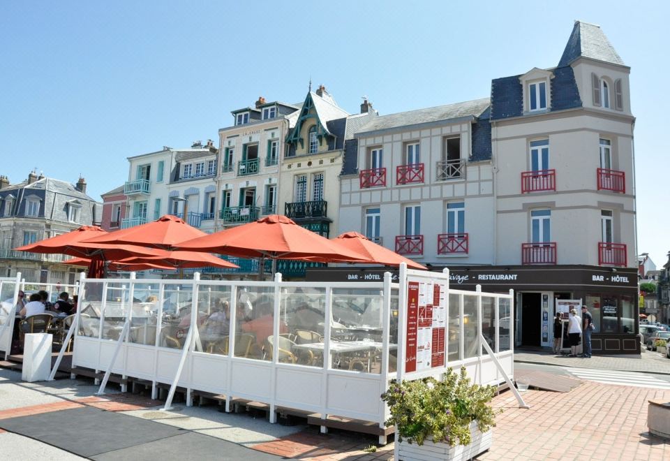 a row of red umbrellas in front of a restaurant with a white building and other buildings in the background at Bellevue Beaurivage
