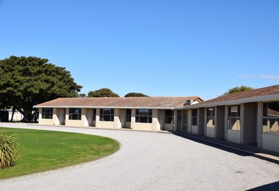 a large , single - story house with a round driveway and a green lawn in front of it at Stansbury Holiday Motel