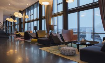 a modern lounge area with multiple chairs and couches arranged in front of large windows at Scandic Narvik