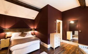 a spacious bedroom with dark red walls , a large bed , and two white dressers in the corner at The Nags Head