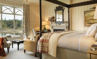 a large bedroom with a four - poster bed , a chair , and a window overlooking a lake at Ballynahinch Castle Hotel