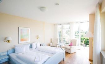 a bedroom with a large bed and white linens , an armchair , and a painting on the wall at Hotel Haus am See