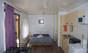 a small , modern bedroom with white walls and wooden floors , containing a bed , desk , and kitchenette at Deniliquin Pioneer Tourist Park