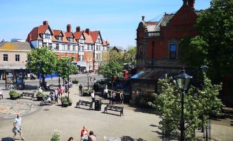 a bustling outdoor café with people sitting at tables , surrounded by trees and buildings in a town square at Mode Hotel Lytham