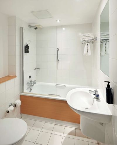a white bathroom with a bathtub , shower , and sink , along with a mirror and towels at Village Hotel Liverpool