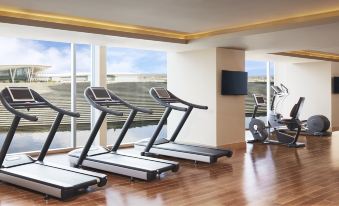 a gym with a row of treadmills and a large tv in the background , overlooking a balcony at Taj Bangalore