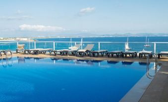 a large blue pool with several lounge chairs and a clear view of the ocean at Hotel Club Sunway Punta Prima