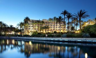 a large building with palm trees and a calm water body in front of it at Parador de Javea