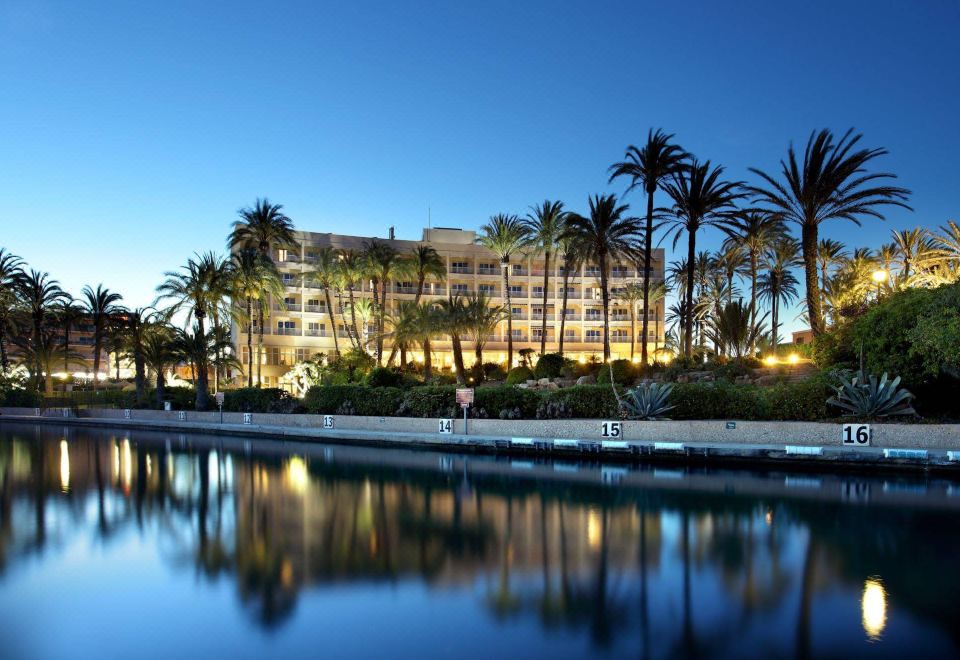 a large building with palm trees and a calm water body in front of it at Parador de Javea