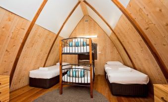 a room with wooden walls and a sloped ceiling has three beds with metal frames at Discovery Parks - Bunbury