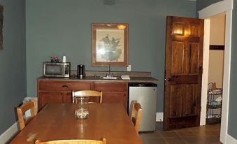 a dining room with a wooden dining table , chairs , and a ceiling fan , as well as a kitchen area with a sink and stove at William Watson Hotel