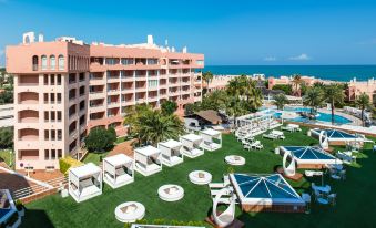 a large hotel with a pool and beach area is surrounded by white lounge chairs and umbrellas at Oliva Nova Beach & Golf Hotel