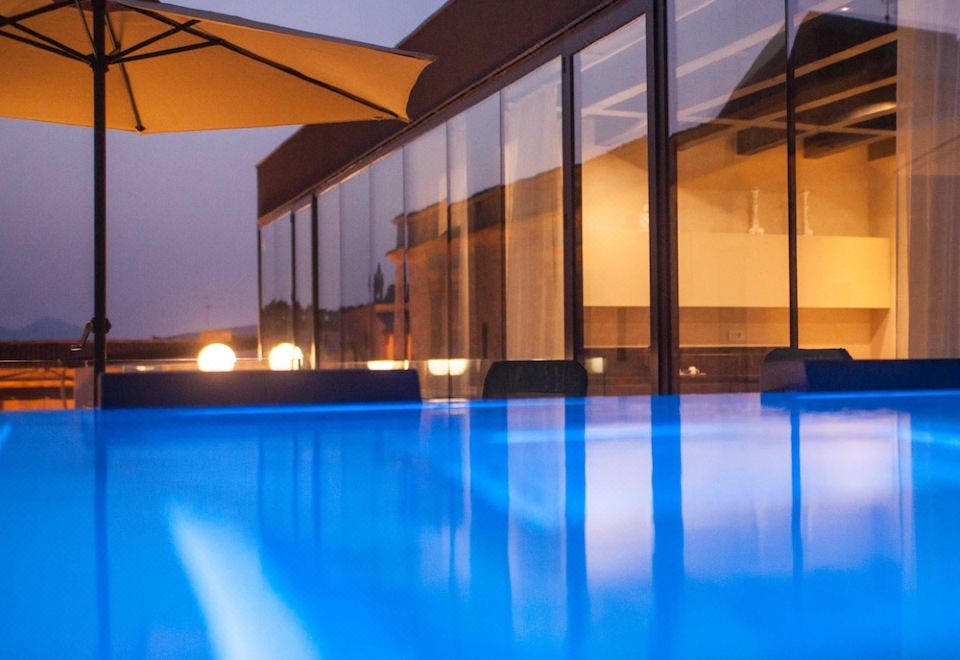 a large blue swimming pool is illuminated at night , with an umbrella and chairs around it at Alba Palace Hotel