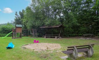 a small wooden cabin in the middle of a grassy field , surrounded by trees and benches at Scout