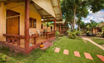 a wooden house surrounded by a lush green lawn , with a pool in the background at Mali Resort Pattaya Beach Koh Lipe