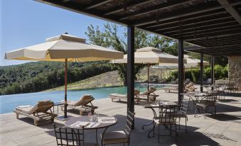 a patio area with several tables and chairs , some of which are under umbrellas , overlooking a pool at Rosewood Castiglion del Bosco