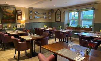 a dining room with wooden tables and chairs , a chandelier hanging from the ceiling , and framed pictures on the walls at Allanton Inn