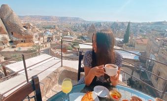 a woman is sitting at a table with food and drinks on it , overlooking a cityscape at Sultan Cave Suites