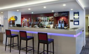 a modern bar with a long counter and red stools , surrounded by various bottles and glasses at Holiday Inn Express Milton Keynes