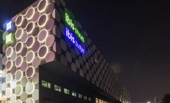 "a nighttime scene of an office building with a sign that reads "" ibis hotel "". several cars parked in the area ,." at Ibis Styles Geneve Palexpo Aeroport