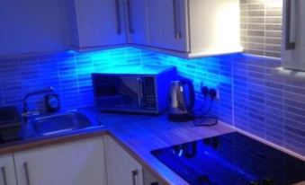 a kitchen counter with blue lights illuminating the top and bottom cabinets , featuring a microwave , sink , and dishwasher at The Port House