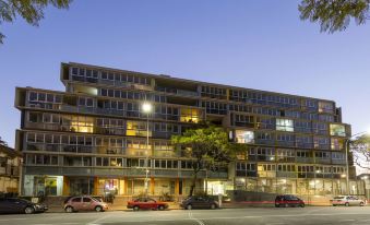 a large apartment building situated on a busy city street , with several cars parked in front of it at IStay Precinct Adelaide