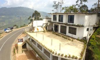 a white building with a parking lot and flower beds on the side of a road , surrounded by mountains at White Home