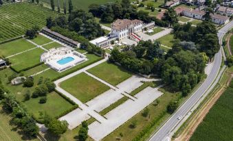 aerial view of a large white house surrounded by green grass and trees , with a swimming pool visible in the background at Hotel Villa Cornér Della Regina