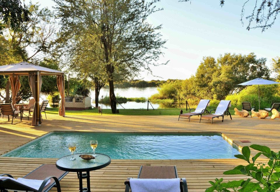 a serene outdoor setting with a swimming pool , sun loungers , and umbrellas , overlooking a serene lake at River View Lodge
