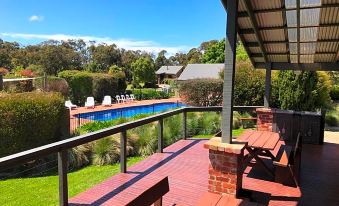 a wooden deck with benches and a view of a pool and surrounding greenery under a clear blue sky at Prom Coast Holiday Lodge