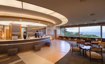 a modern reception area with a curved counter , seating area , and large windows overlooking the outdoors at Kamenoi Hotel Atami Annex