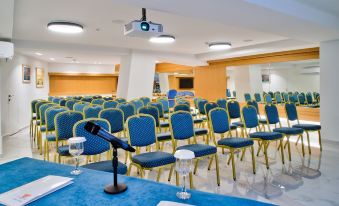 a large conference room with rows of blue chairs arranged in a semicircle , and a projector on the wall at Poseidon Hotel