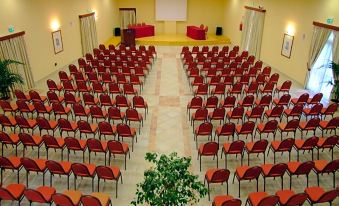 a large conference room with rows of red chairs and a projector screen at the front at VOI Arenella Resort