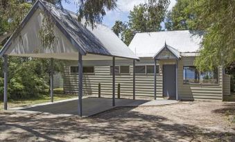 a small , two - story house with a covered porch and metal roof is nestled in the woods at Waterfront Retreat at Wattle Point